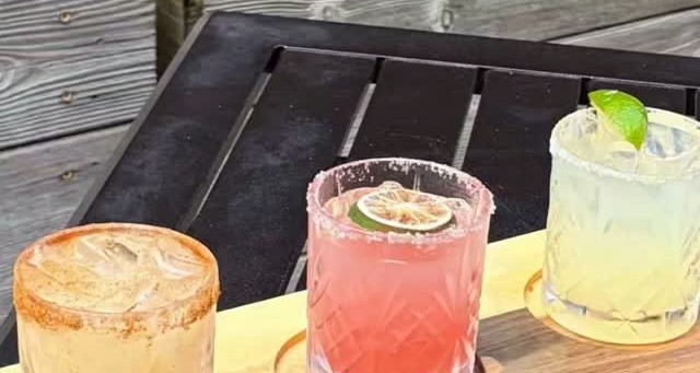 Three margarita flight glasses on a wooden paddle at the patio